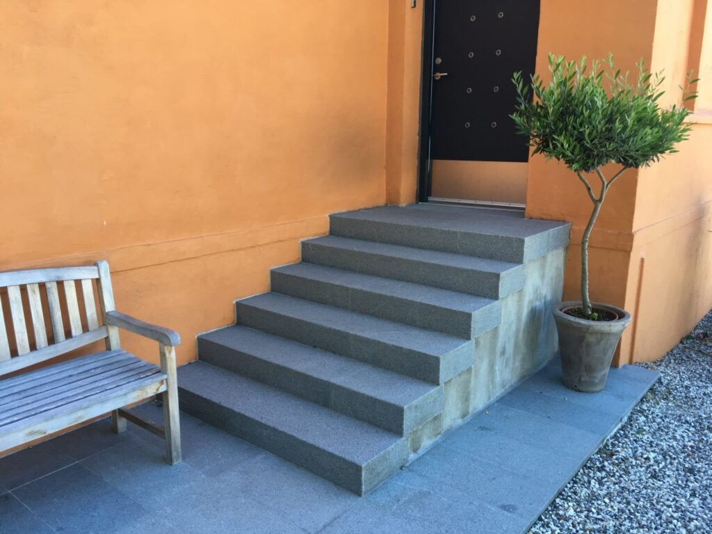 Grå trappe ved orange væg med bænk og plante