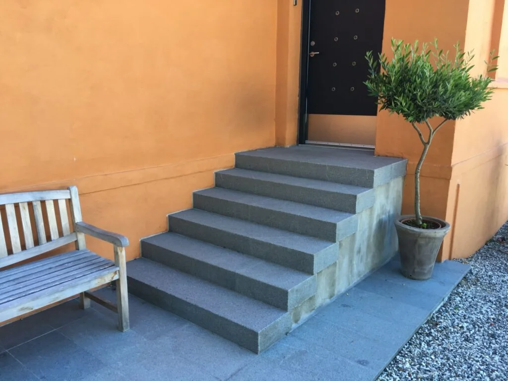 Grå trappe ved orange væg med bænk og plante